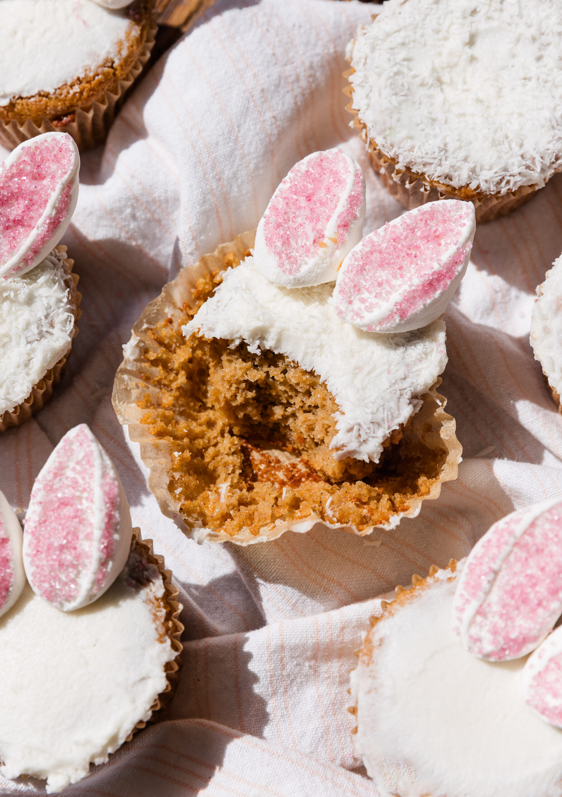 Vanilla cupcake with big bite taken out topped with white frosting and marshmallow bunny ears.
