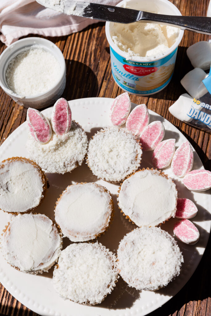 All vanilla cupcakes frosted on a white plate with frosting and shredded coconut on the side.