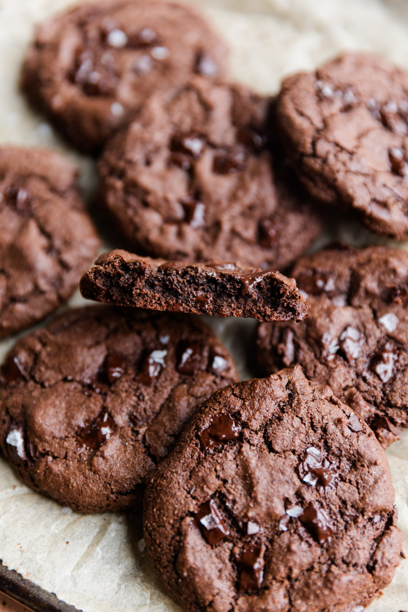 Double chocolate chip cookies on a parchment paper lined baking sheet with one cut in half so you can see the gooey inside.