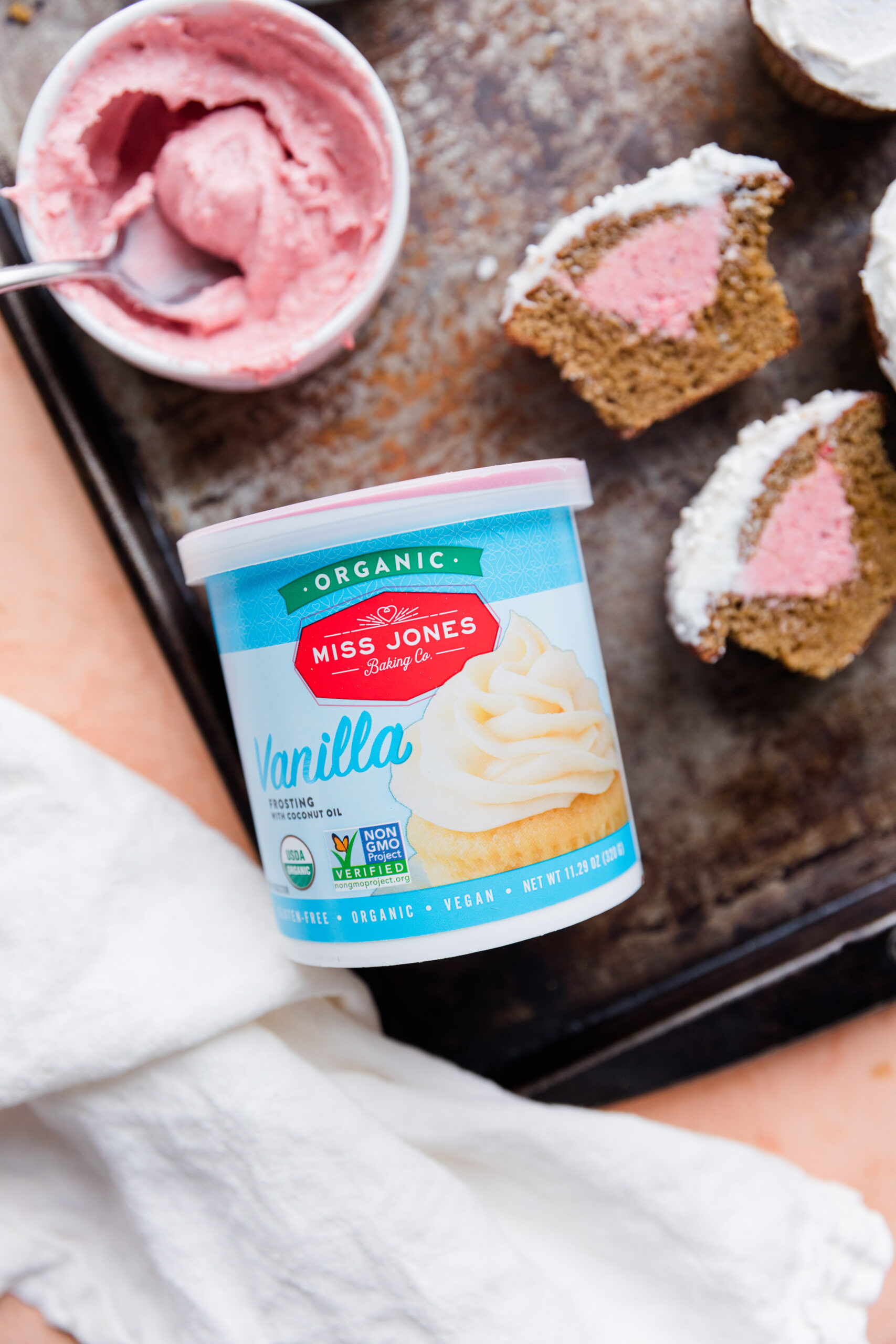 Naturally dyed pink strawberry frosting in a bowl with pink gender reveal cupcakes and dairy free vanilla frosting.