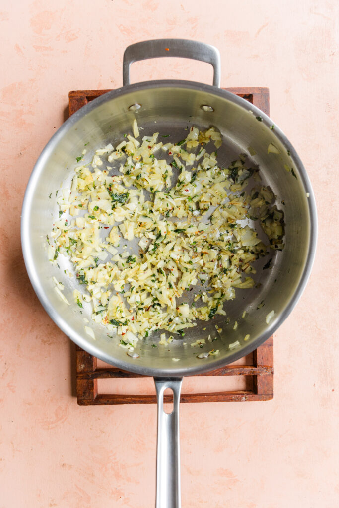 Onions cooking with garlic, red pepper flakes, fresh basil, and olive oil in large pan.