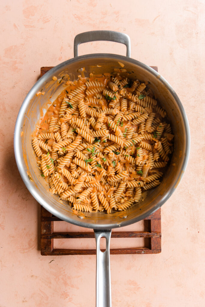 Gluten-free pasta mixed in with pink pasta sauce in large pan.