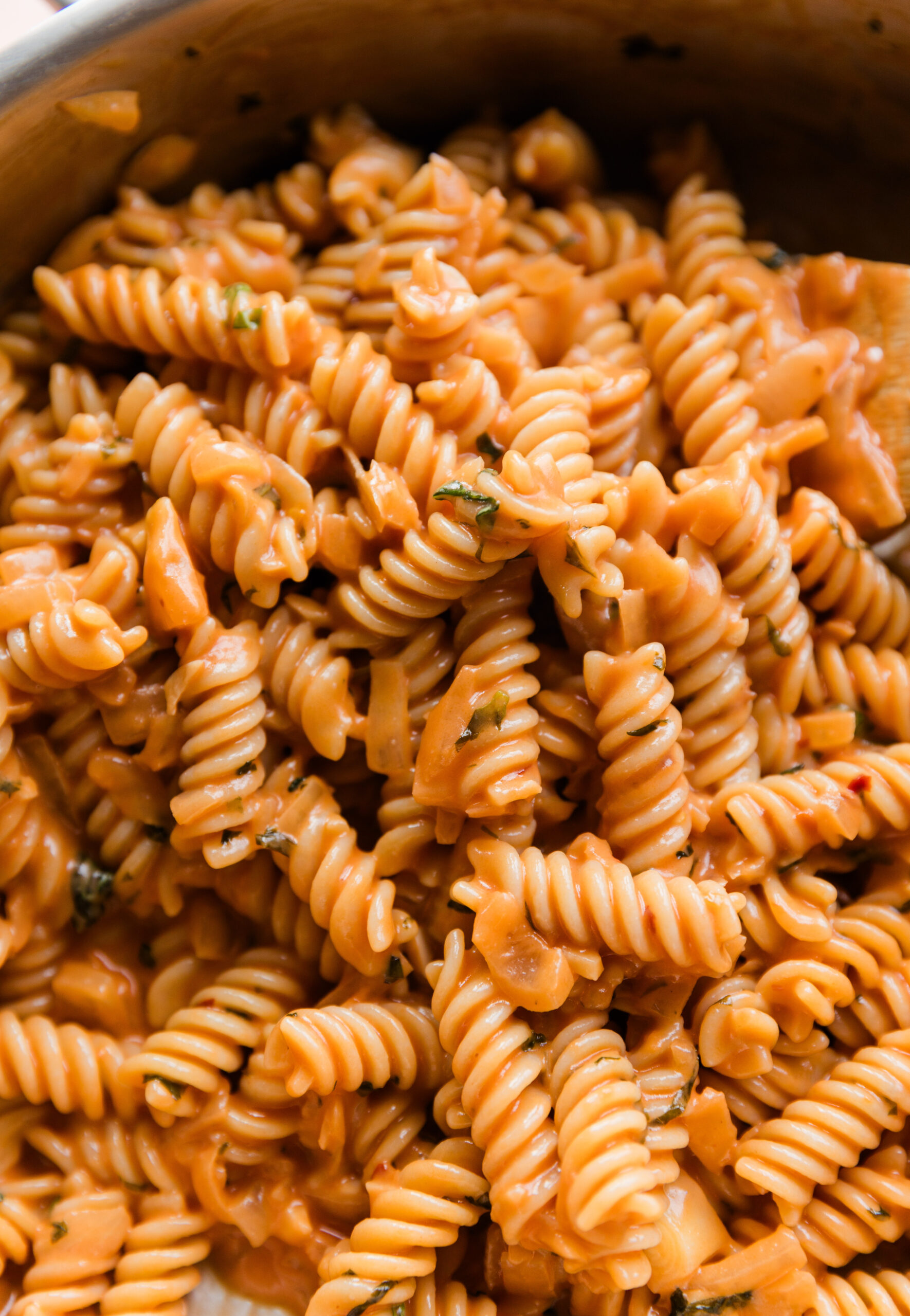 Pink pasta sauce on gluten-free noodles in a pot.