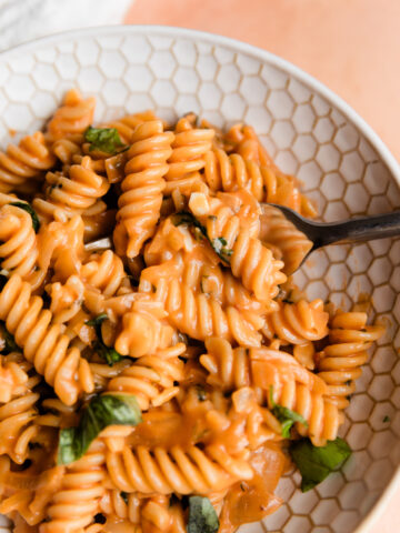 Close up picture of pink sauce pasta in white bowl with a fork.