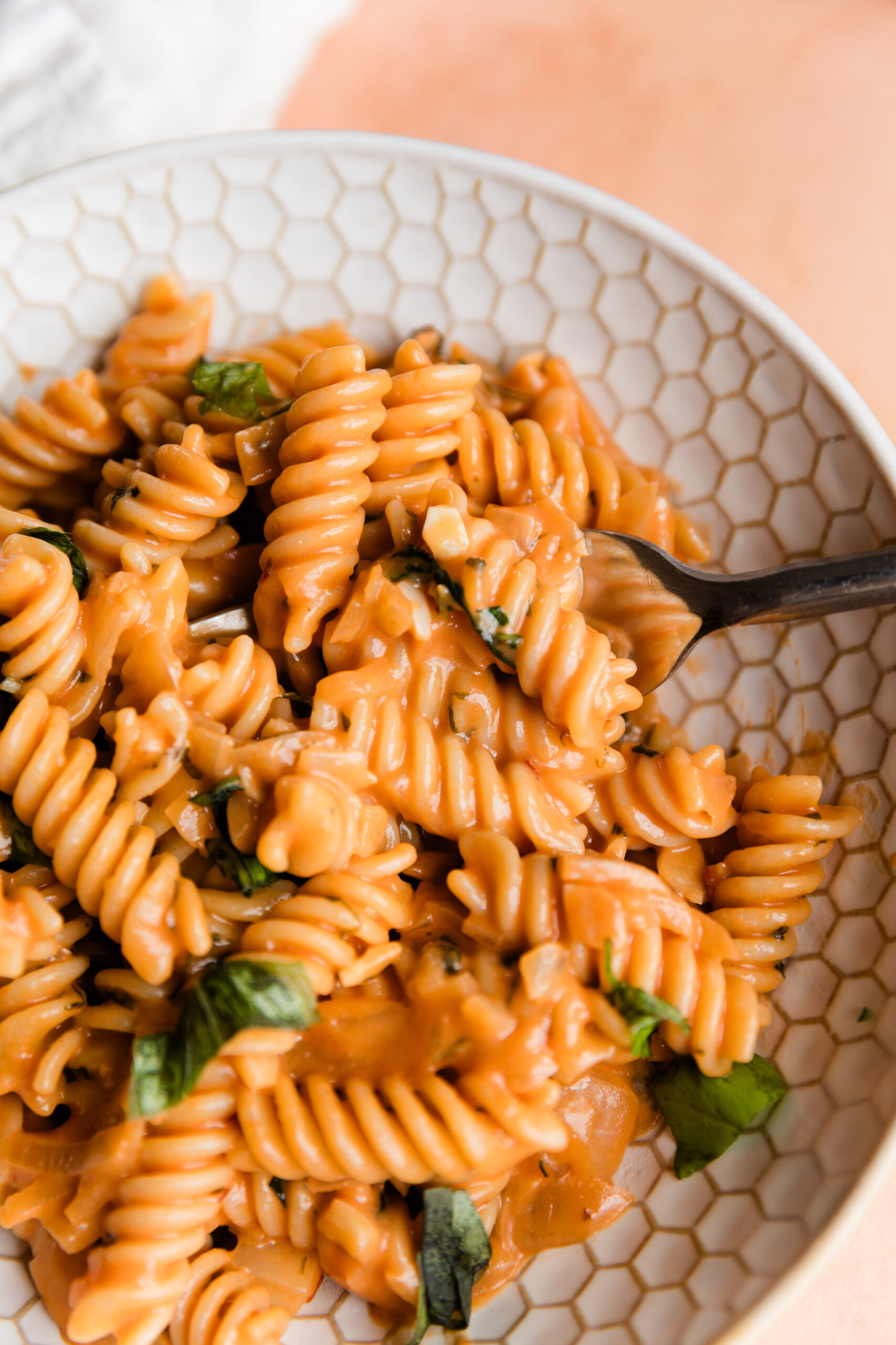 Close up picture of pink sauce pasta in white bowl with a fork.