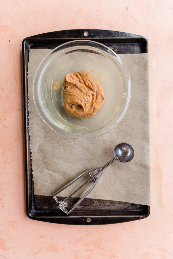 Nut butter filling mixture in bowl on a parchment paper lined baking sheet with a small cookie scoop.