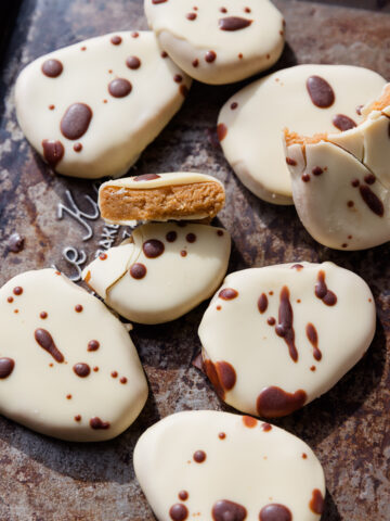 White chocolate covered copycat healthier Reece's eggs on a baking sheet with dark chocolate drizzled on top.