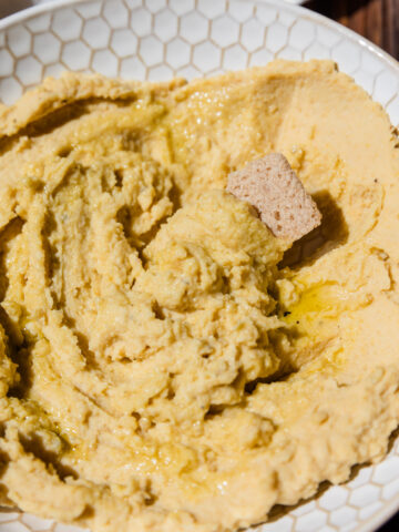 Creamy homemade hummus with a cracker scooping out a bite.