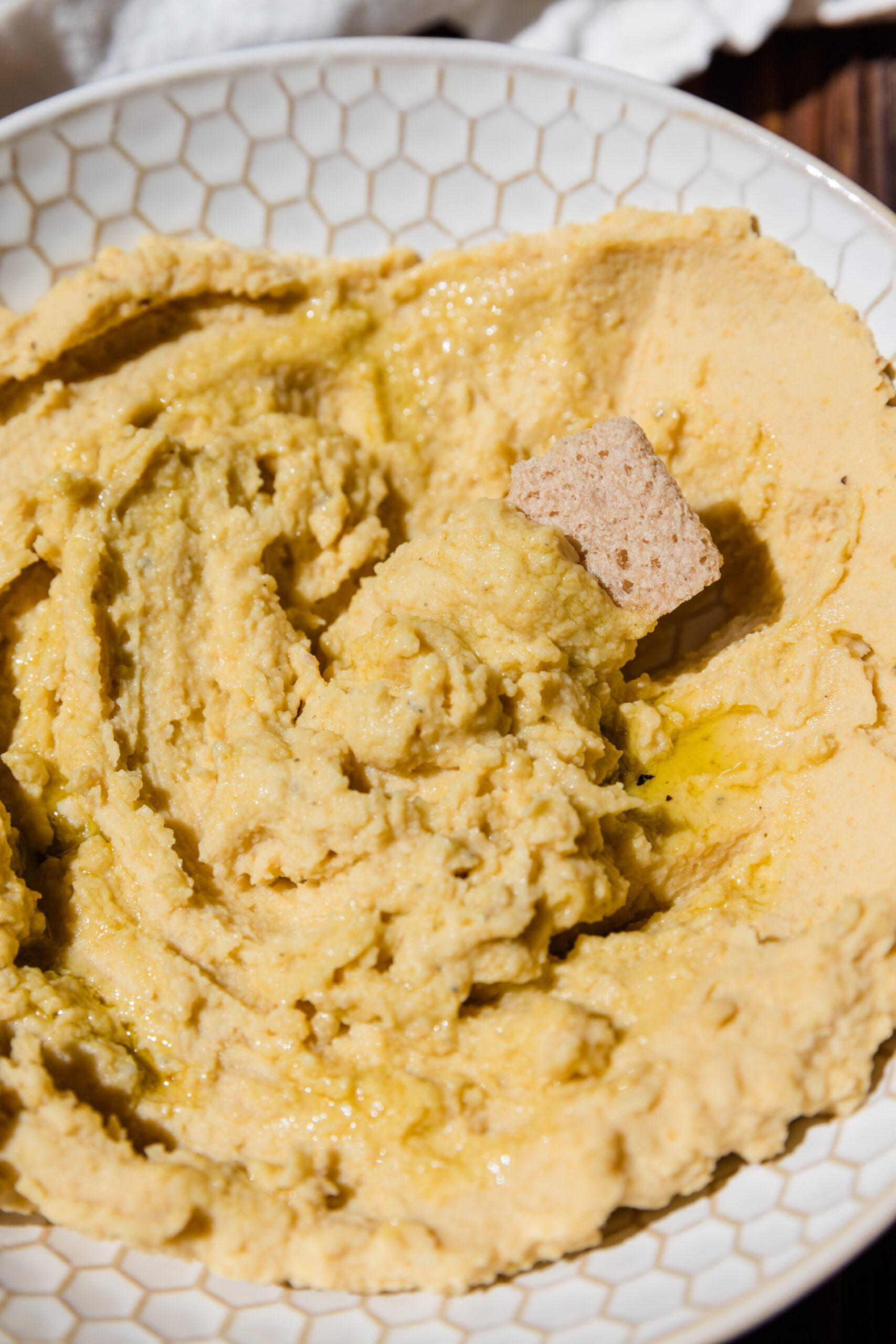 Creamy homemade hummus with a cracker scooping out a bite.