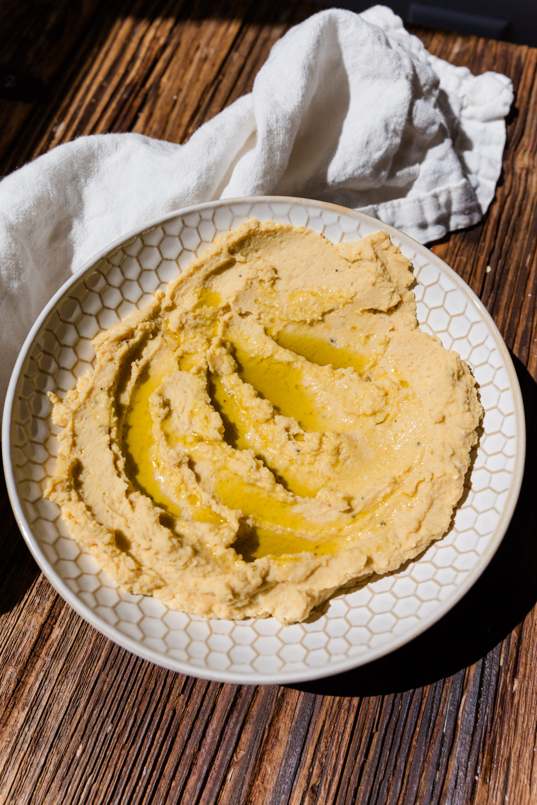 White bowl with creamy homemade hummus topped with olive oil.